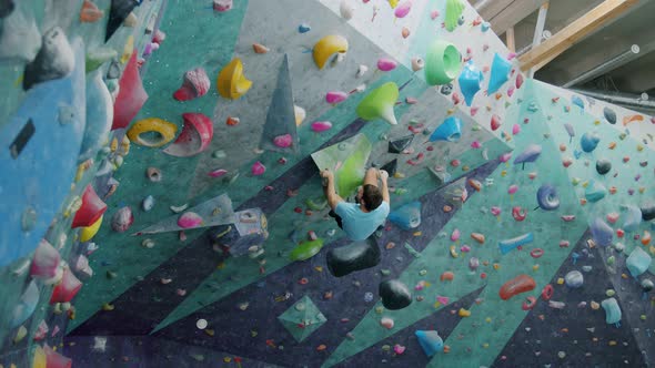 Guy Climbing Up Artificial Wall Then Falling on Crash Mat in Indoor Sports Facility alt