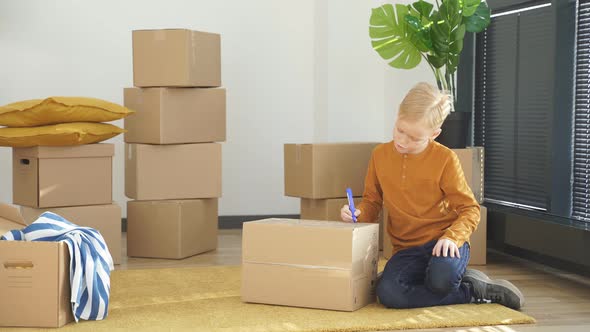 Boy Surrounded By Boxes in an Old Apartment Signs a Box and Prepares to Move