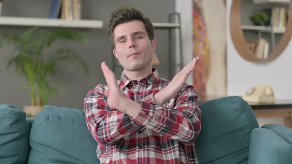 Portrait of Man Showing NO Sign By Arm Gesture Sitting on Sofa alt