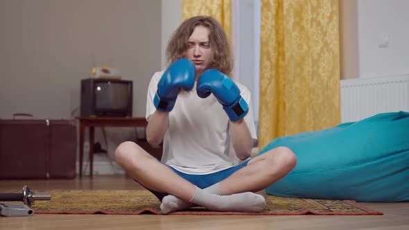 Young Skinny Man with Long Curly Hair Sitting on Retro Carpet in Boxing Gloves Fighting Shadow and alt