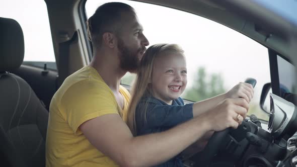 Side View of Happy Father Kissing Head of Laughing Little Daughter Imitating Riding Turning Steering alt