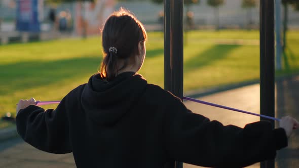 Young Woman is Doing Physical Exercise with Elastic Band in Park alt