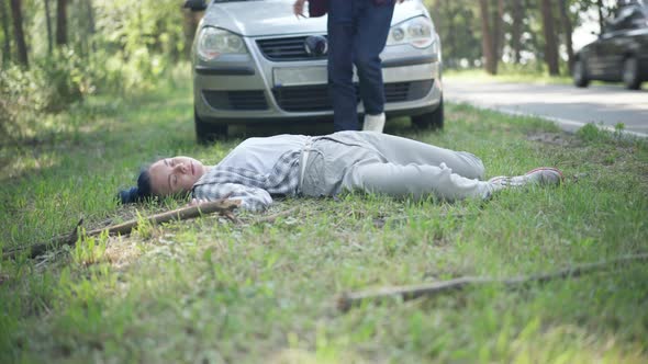 Wide Shot Knocked Down Woman Lying on Roadside with Man Walking Out the Car Checking Corpse Pulse alt