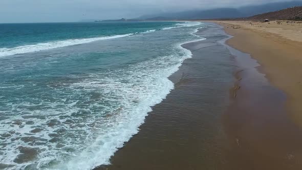 one side the ocean the other the sandAerial shot moving forwards along the waves alt