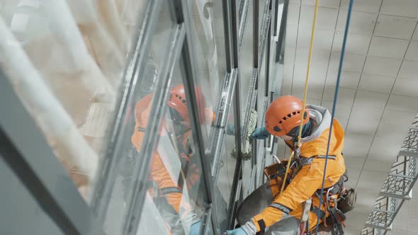 Industrial Climber in Helmet and Gloves Washes Windows on Tall Building Top View alt