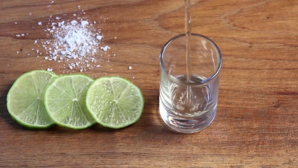 Pouring Tequila In Glass With Lime Slices And Salt