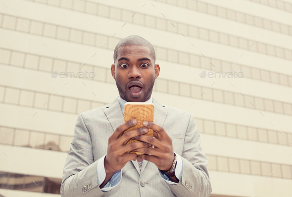 shocked young business man looking at phone seeing bad news