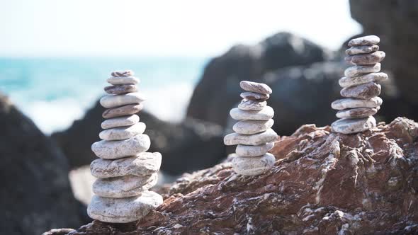 Three Balanced Pyramids of Stones on the Beach on the Background of Sea Waves alt
