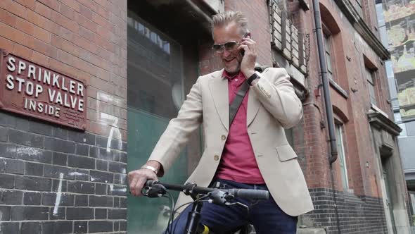 Happy businessman on bicycle in London having phone call