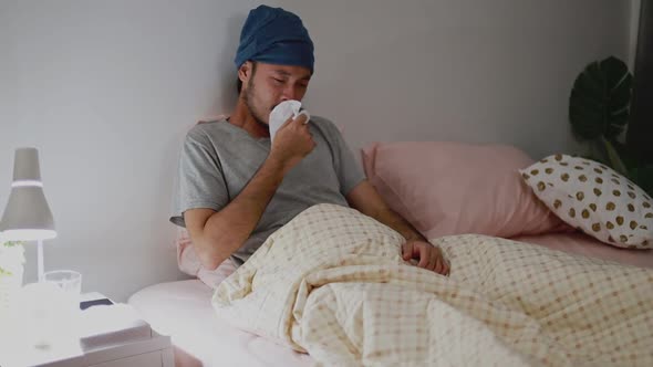 Asian man coughs sick while in the bedroom at home.