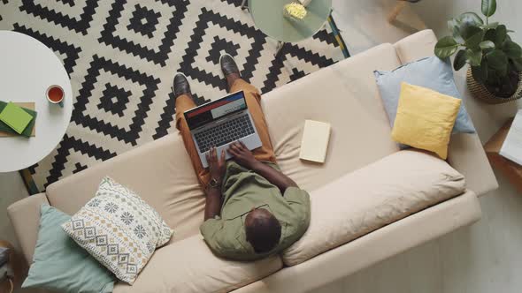 Black Man Using Laptop on Sofa in Living Room alt