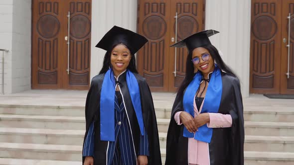 Two AfricanAmerican Women Graduates in Classic Master's Suits and Robes Stand in Front of the alt