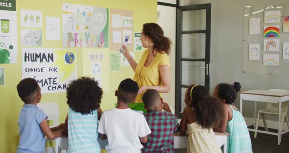 Video of happy caucasian female teacher and class of diverse pupils studying ecology in classroom alt