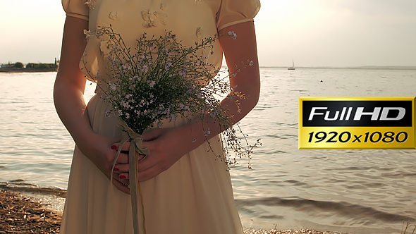 Romantic Young Woman With Field Flowers Near The Water At Sunset