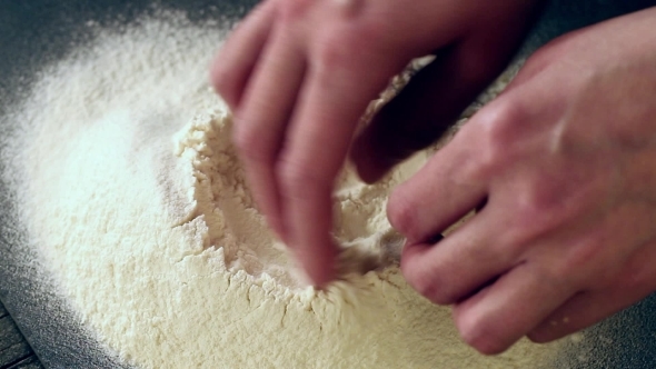 Female Hands Break The Egg Into Flour For Making Dough Over Black Table