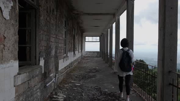 Back view of woman walking on long balcony of Caramulo Sanatorium old abandoned building. Static vie alt