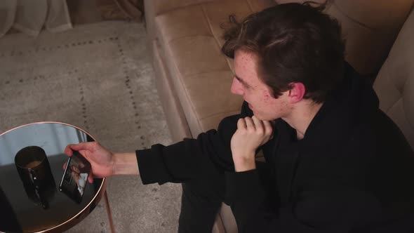 Man Has Video Call Chatting on Phone with Friends Sitting on Couch at Home alt