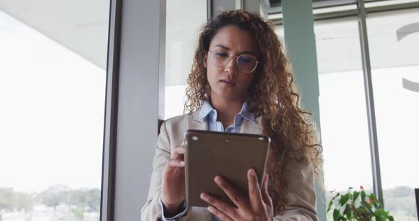 Biracial businesswoman sitting by desk and using tablet in modern interiors alt