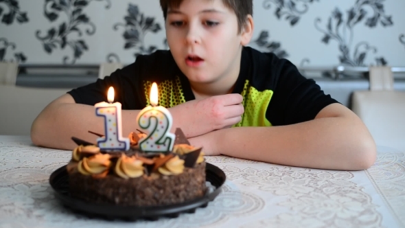 The Boy Blowing On  Cake Candles  With  Number Twelve