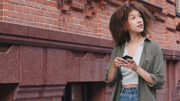 Happy African American Woman Holding Phone Using Digital Assistant on Smartphone Sets Course Finds alt
