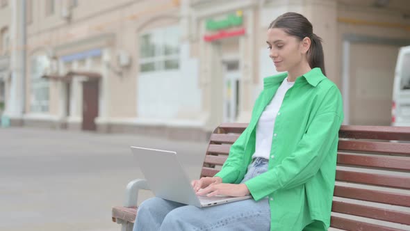 Hispanic Woman with Laptop Smiling at Camera While Sitting Outdoor on Bench alt