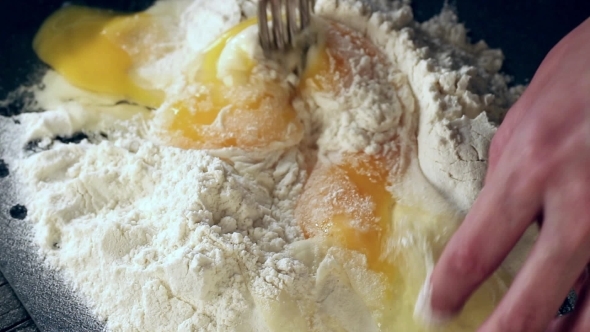Female Hands Knead Eggs In Flour For Making Dough Over Black Table
