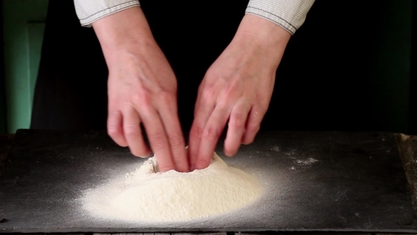 Female Hands Break The Egg Into Flour For Making Dough Over Black Table