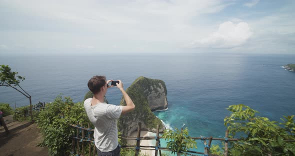 Back Ascending View of a Male Tourist Taking Pictures of the TRex Bay Peninsula at Kelingking Beach alt