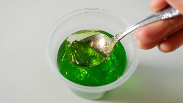 Lady's Hands Using Spoon To Scoop Green Jelly  on Dining Table