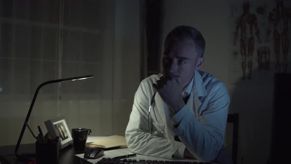 Depressed Doctor Working At His Office Desk alt