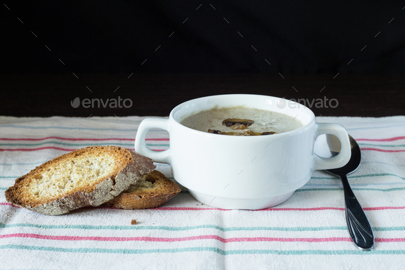 Bowl of mushroom soup with bread on wooden board