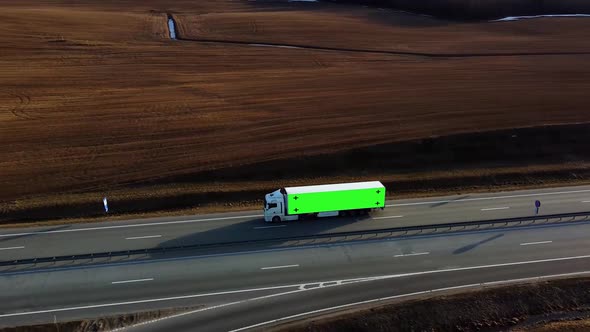 Truck with green screen on trailer drives along the highway in the rays of the setting sun. alt