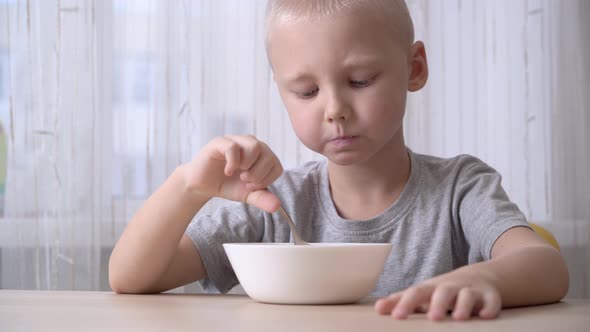 Cute satisfied little boy eating cornflake with milk for breakfast. alt