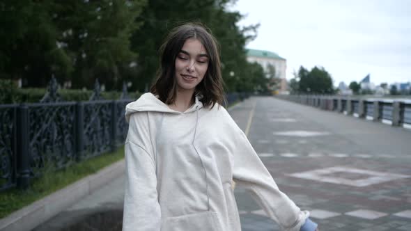Smiling Girl in a White Hoodie, Walks Along the River Embankment