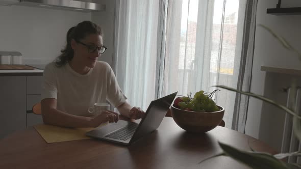 Happy woman sitting in the kitchen and chatting with her laptop