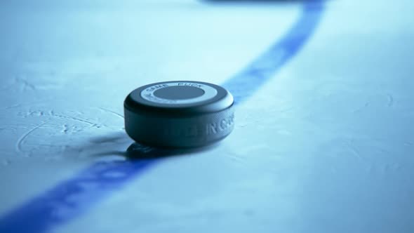 Hockey Stick shoots a black rubber puck on a rink arena from marking line.