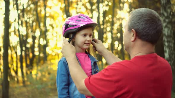 Dad helps the girl to put on a safe helmet before riding a bike on a Sunny autumn day in nature