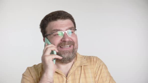 Man with a beard and glasses is happily talking on a smartphone on a gray background alt