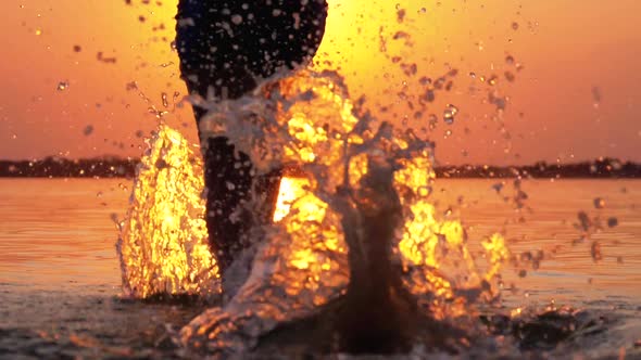 Silhouette of Legs of Boy Running Into the Water at Sunset and Creating Splashes. Slow Motion alt