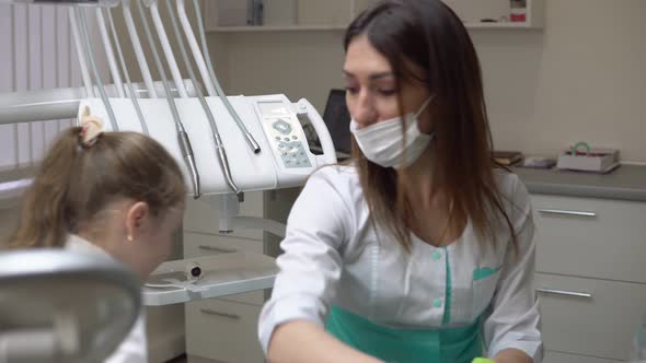 Friendly Female Dentist Taking Off a Napking After Procedures and Giving Cute Little Girl a alt