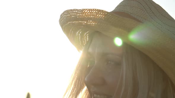 Face of an Attractive Young Woman in a Summer Hat Against the Backdrop of the Sun alt