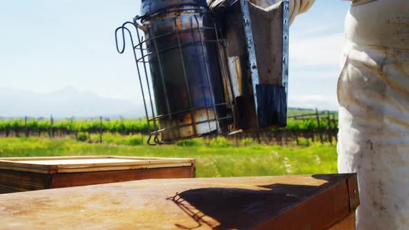 Close-up of beekeeper keeping bee smoker on honeycomb box alt