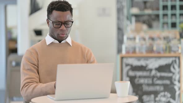 Creative African Man Coughing While Using Laptop in Cafe alt