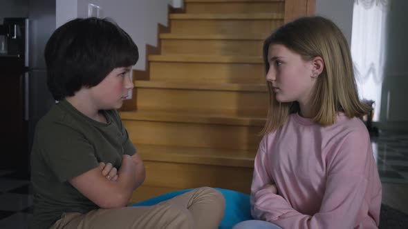 Side View Argued Brother and Sister with Crossed Hands Looking at Each Other Sitting on Bag Chair in alt