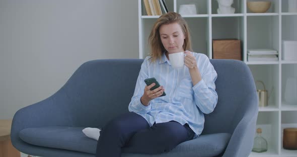 Attractive Redhair Teenager Girl Sitting of the Sofa at Home Using Phone and Smiling. Feeling Happy alt