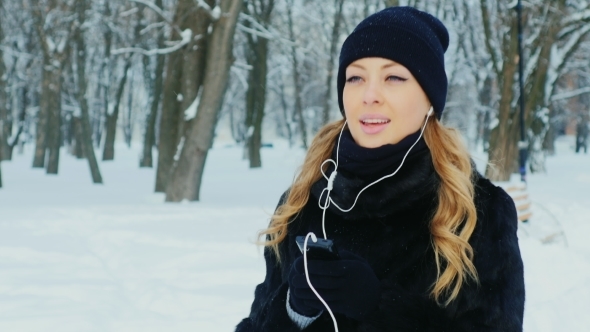 Attractive Woman Walking In a Winter Park, Listening To Music On Headphones alt
