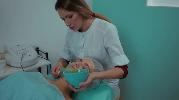 the Beautician Conducts the Procedure Applies a Green Mask to the Woman's Face