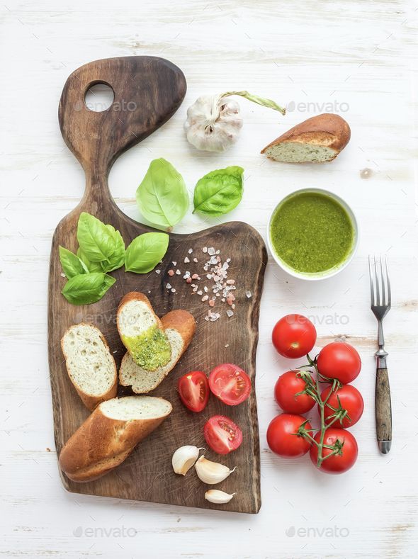 Pesto sauce, bread, cherry-tomatoes, fresh basil and garlic on rustic walnut chopping board - Stock Photo - Images