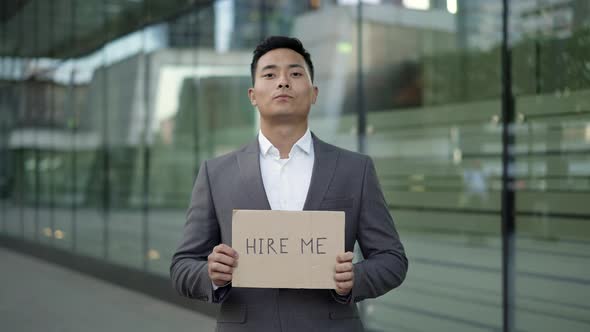 Left To Right Pan Real Time Shot of a Young Asian Man in a Suit Standing on the Street with a Sign alt