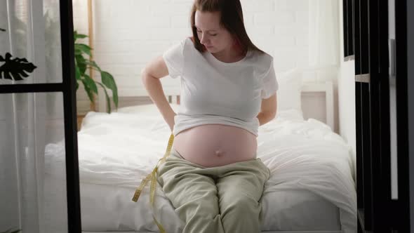 Young Woman Measuring Her Pregnant Belly with Centimeter Tape alt